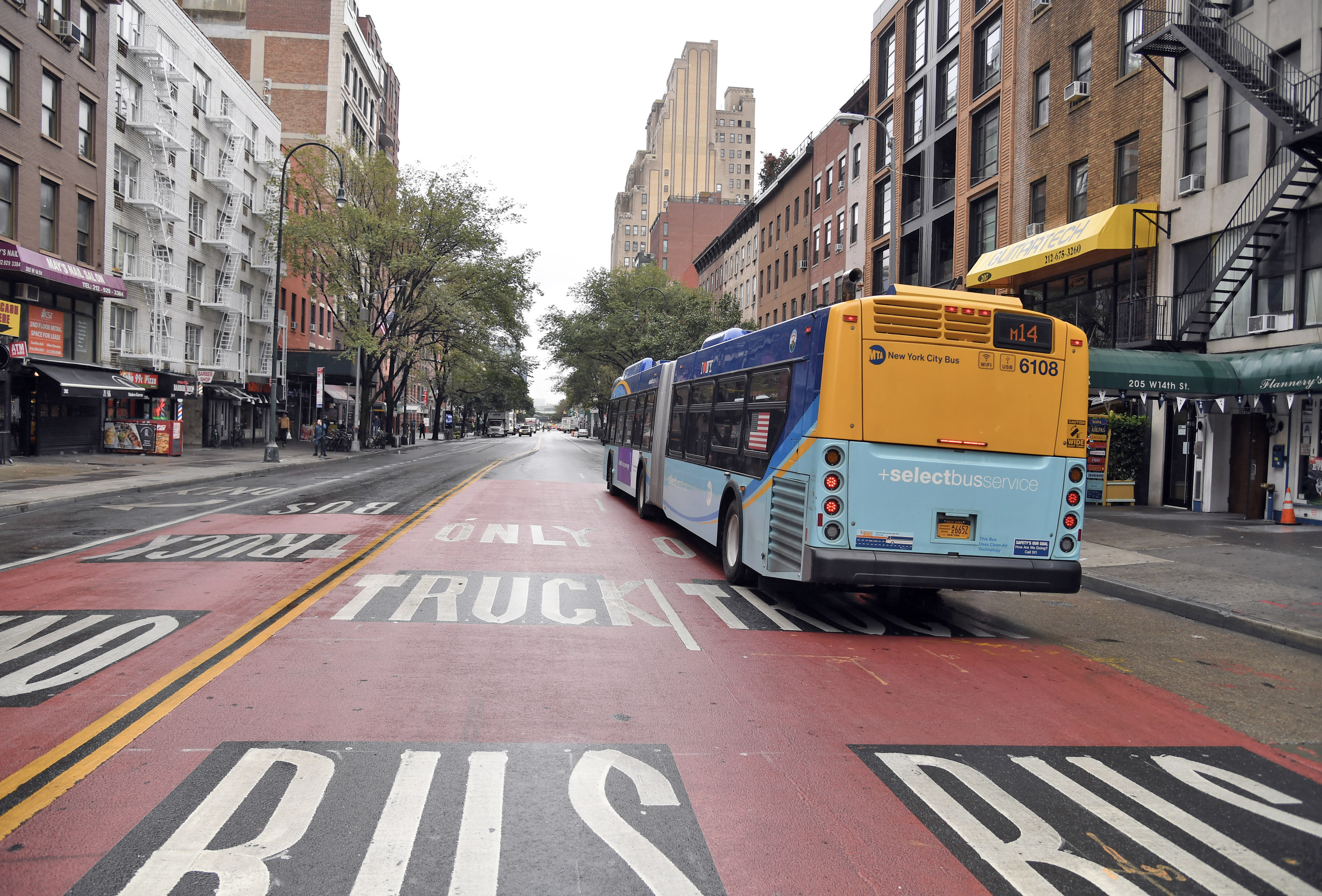 A blue and yellow bus with a “Select Bus Service” decal drives down a road painted red and marked "bus only." 