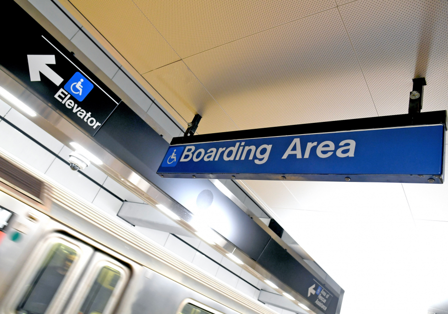 A blue sign with the words "Boarding area" and an icon showing a person in a wheelchair. On a different sign on the left is the same icon and an arrow pointing toward elevators.