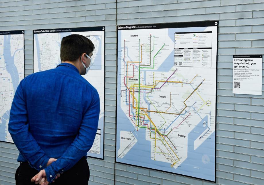 A man in a blue shirt looks at a subway diagram that has been installed on the wall of a subway station.