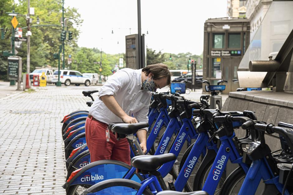 A man selects a blue Citi Bike from a bike-share station near a subway stop.
