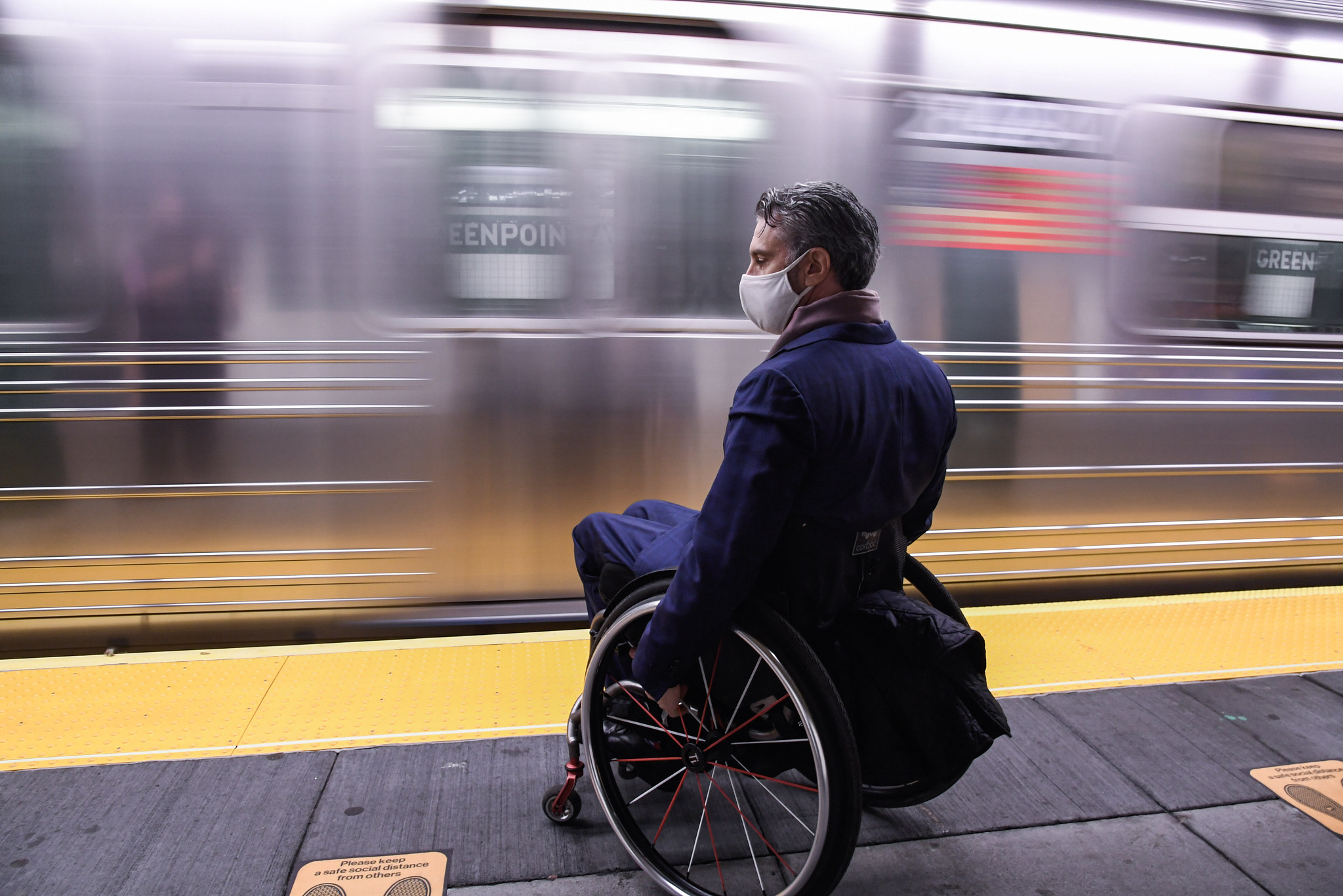 Man in wheelchair waits for train at platform, train moving in background