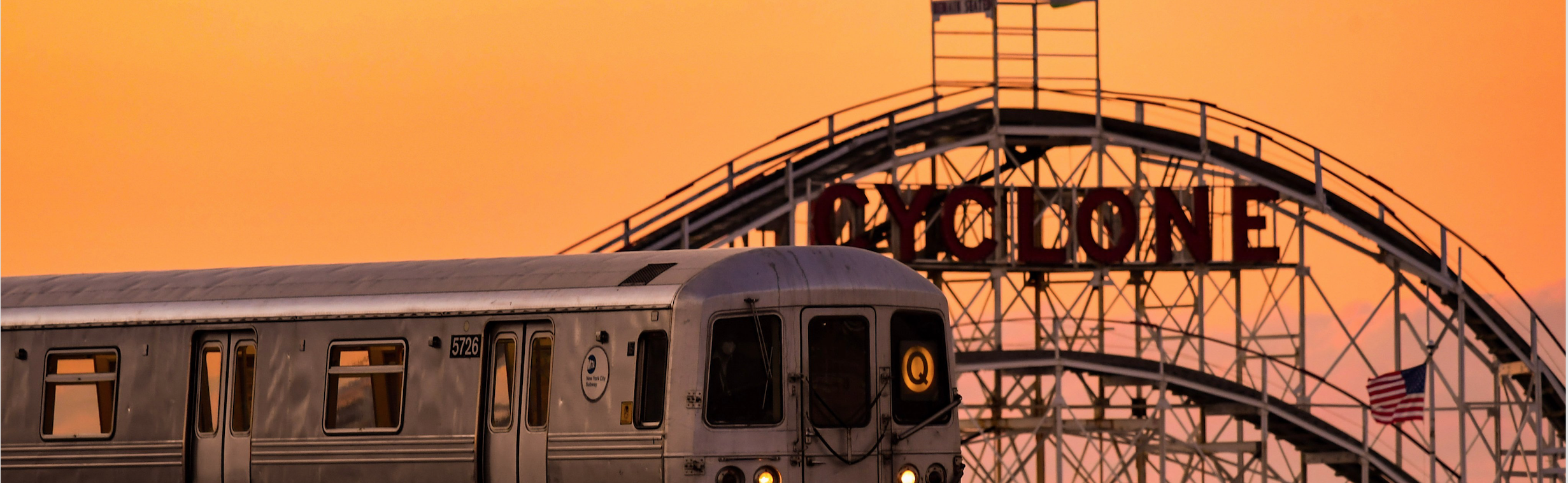 Q train passing the wooden Cyclone roller coaster during orange Coney Island sunsent