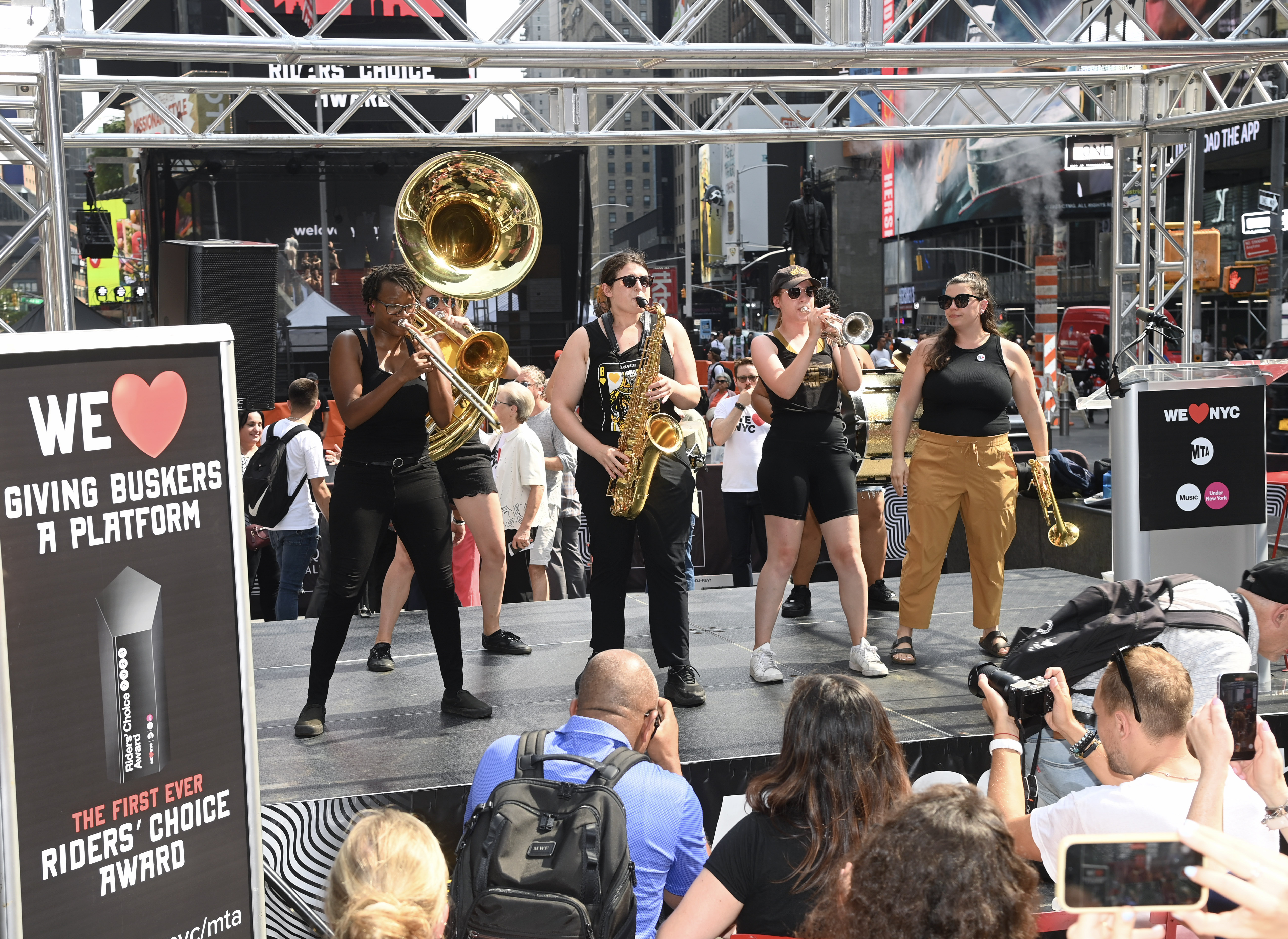 A group of women performing on a stage with brass instruments.