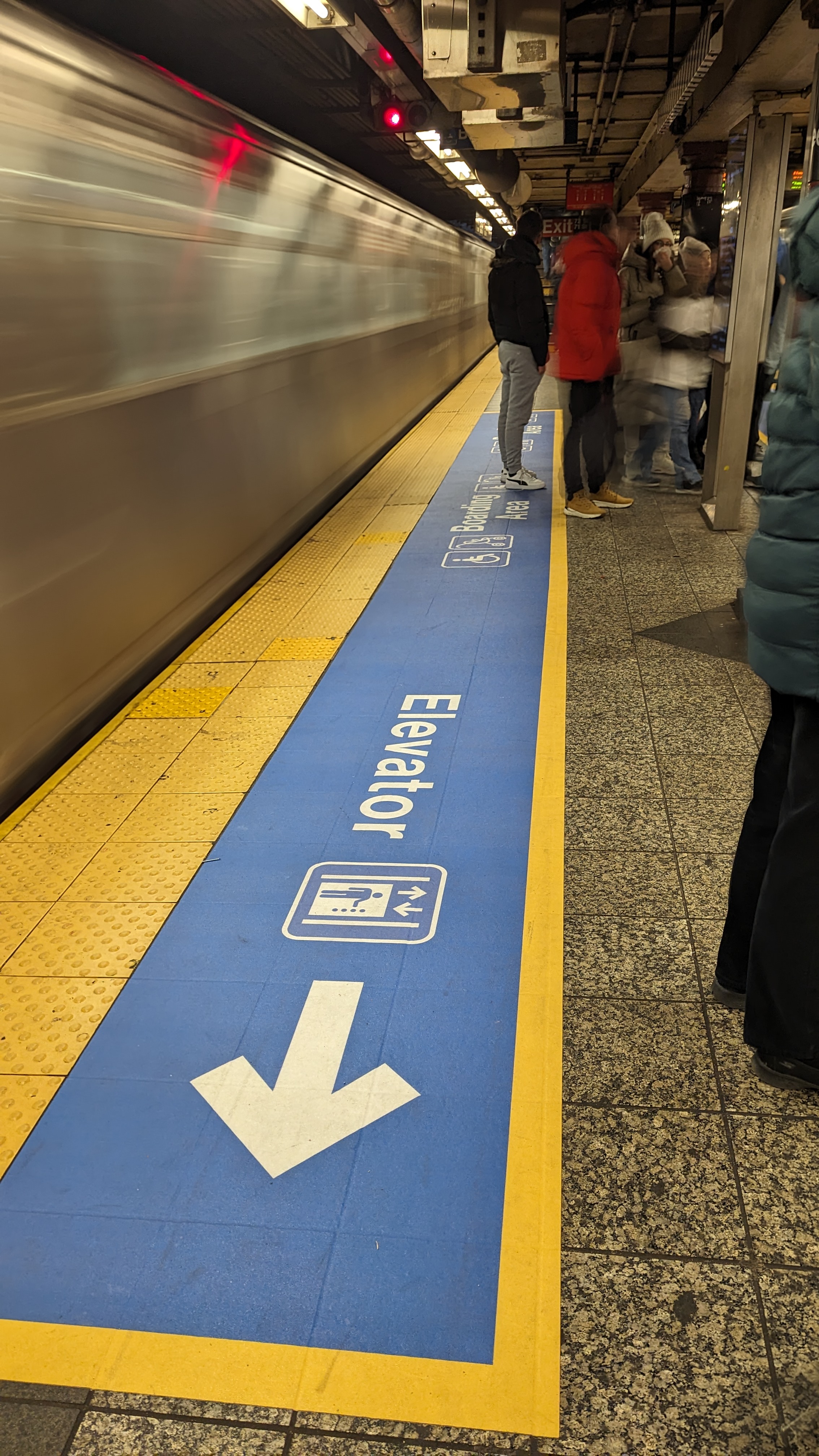 Blue decal with yellow boarder at a platform edge. The decal includes boarding area designation and an arrow pointing towards the elevator.