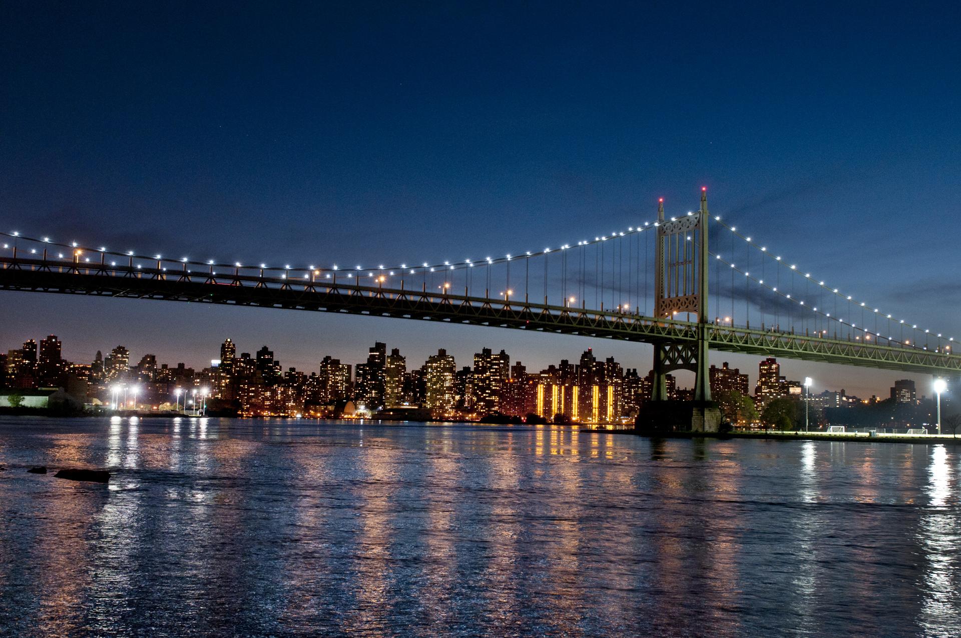 A bridge illuminated at twilight stretches over a view of the lit-up cityscape.