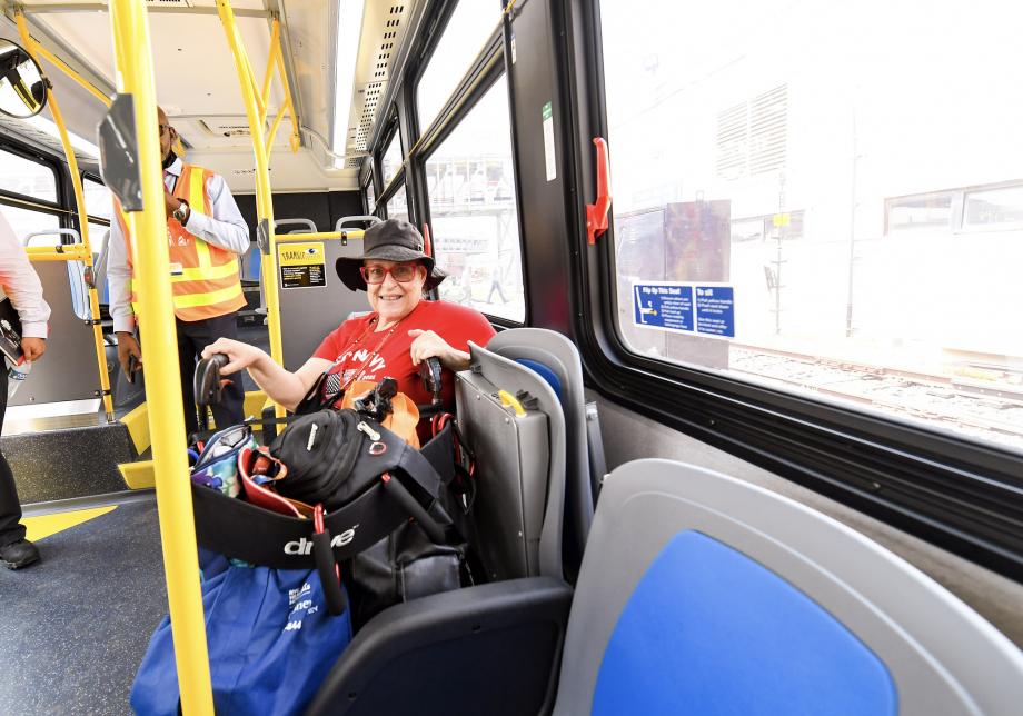 A woman using a wheelchair sits on a bus with blue and gray seats. 