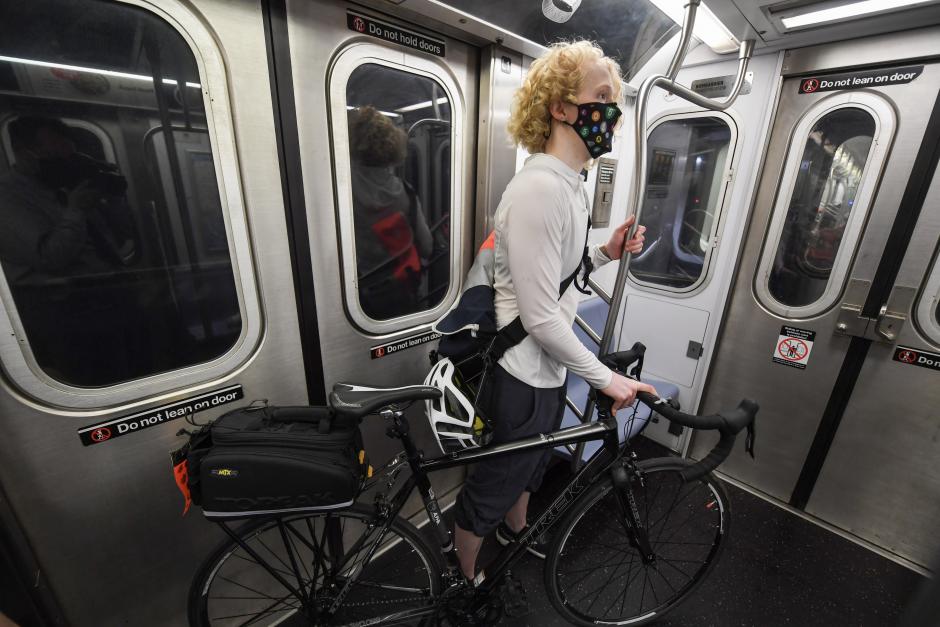A woman stands with her bike at the end of a subway car. She's holding onto one of the stanchion poles. Subway seats are visible to her left.