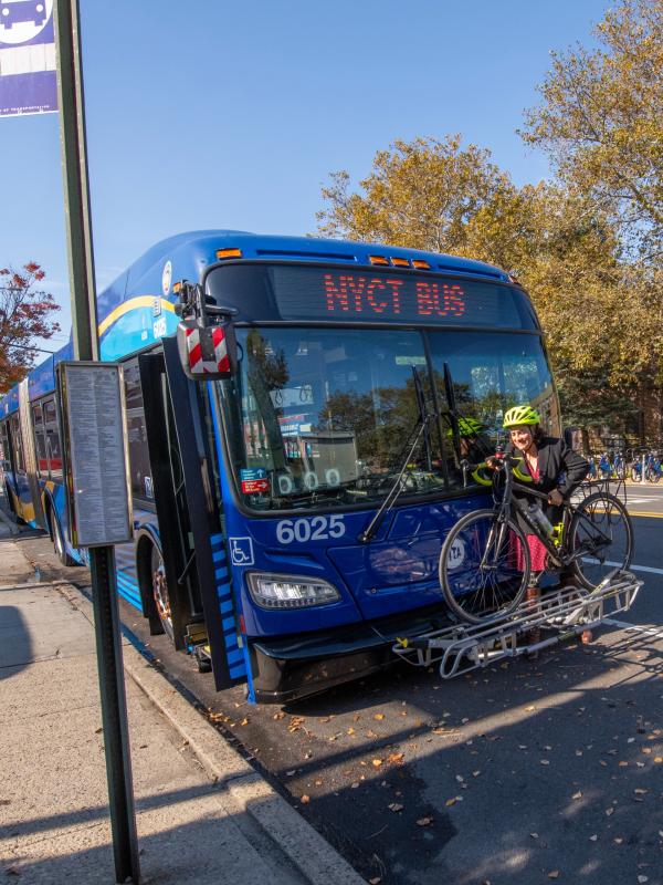 A person in a bike helmet lifting their bicycle onto the bike rack of a bus 
